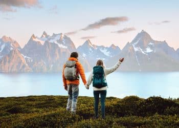 Couple with backpacks admiring breathtaking Nordic mountain landscape by the water, representing the best Nordic country to visit for nature lovers