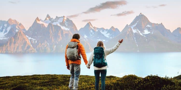 Couple with backpacks admiring breathtaking Nordic mountain landscape by the water, representing the best Nordic country to visit for nature lovers