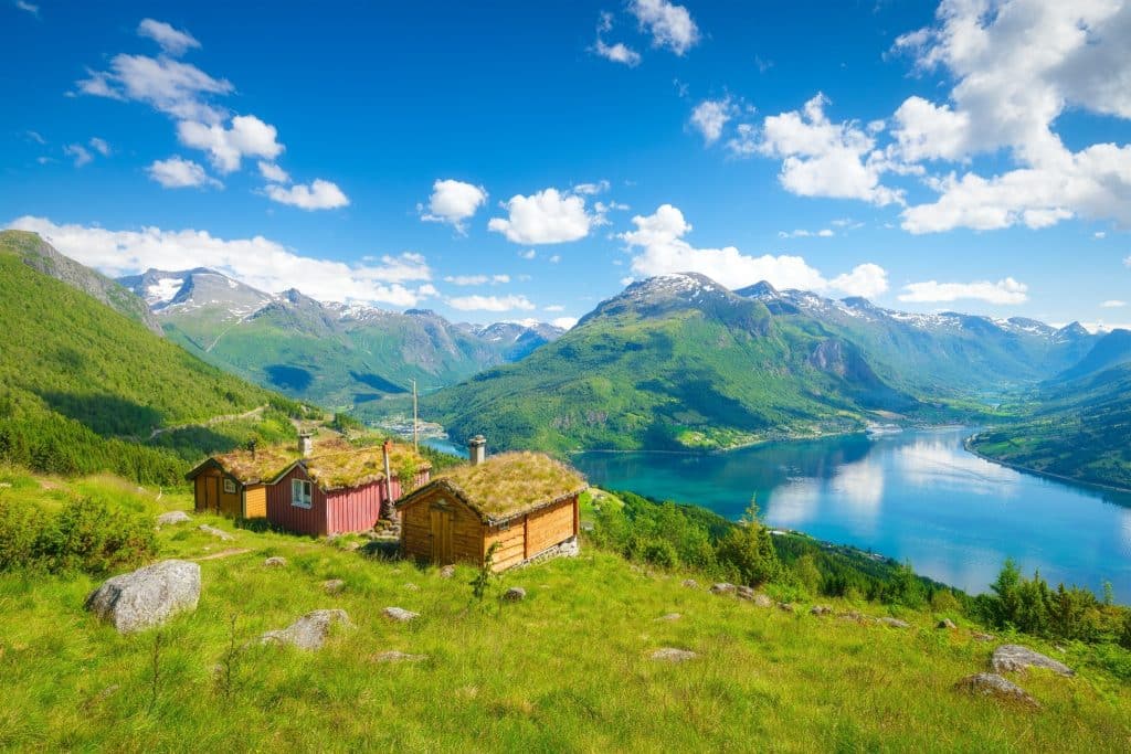 Traditional wooden cabins on a hillside overlooking a stunning scenery and mountains, capturing the natural beauty of the best Nordic country to visit.