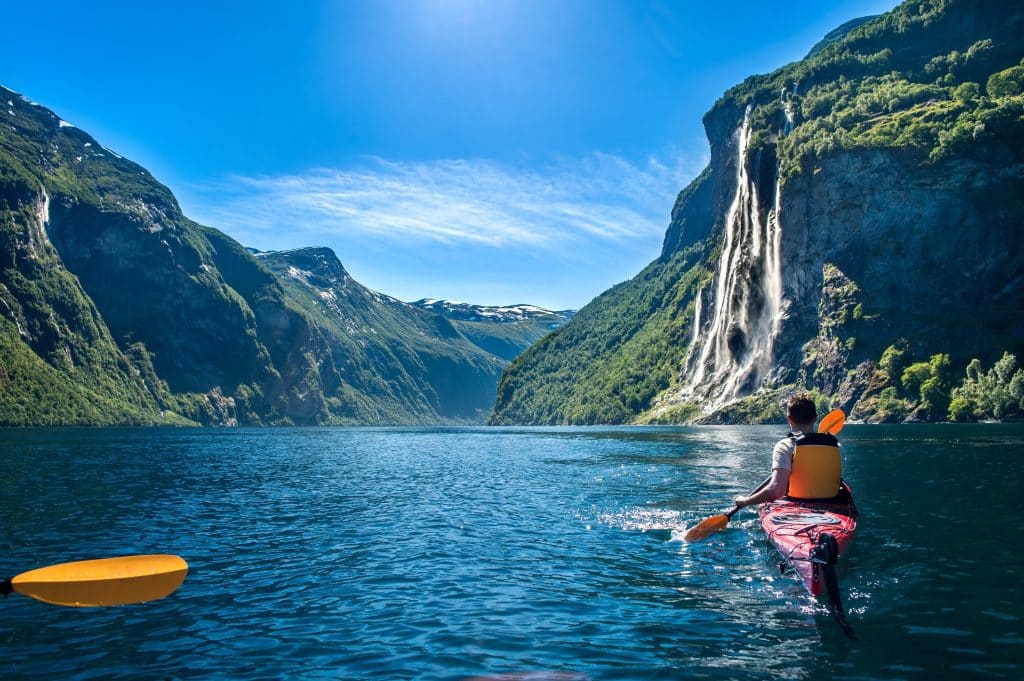 Kayaker paddling through a dramatic Nordic river with a tall waterfall, capturing the adventure and scenery of the best Nordic country to visit.