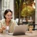 Smiling woman working remotely at an outdoor café with her laptop, representing modern places to work remotely near me with a relaxed atmosphere.
