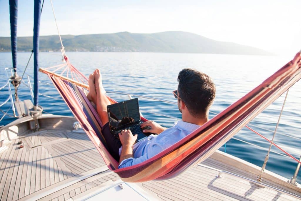 Remote worker using a laptop in a hammock on a sailboat, showing creative and scenic places to work remotely near me.
