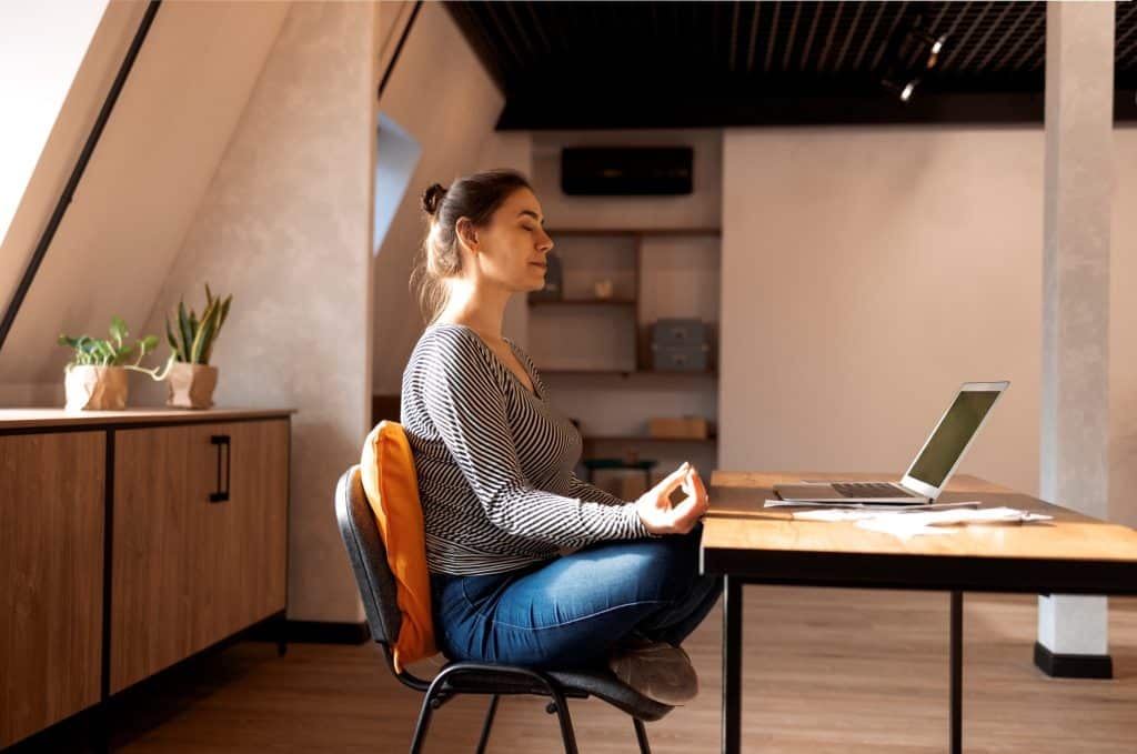 Freelancer practicing mindfulness meditation at her home office desk, a healthy habit in the daily routine freelancer lifestyle.