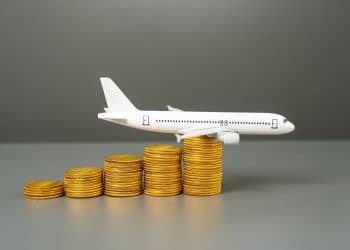 Model airplane on stacked coins symbolizing how flight booking hacks like comparing ticket prices in different currencies help travelers save money.