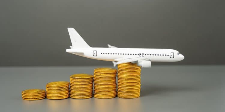 Model airplane on stacked coins symbolizing how flight booking hacks like comparing ticket prices in different currencies help travelers save money.
