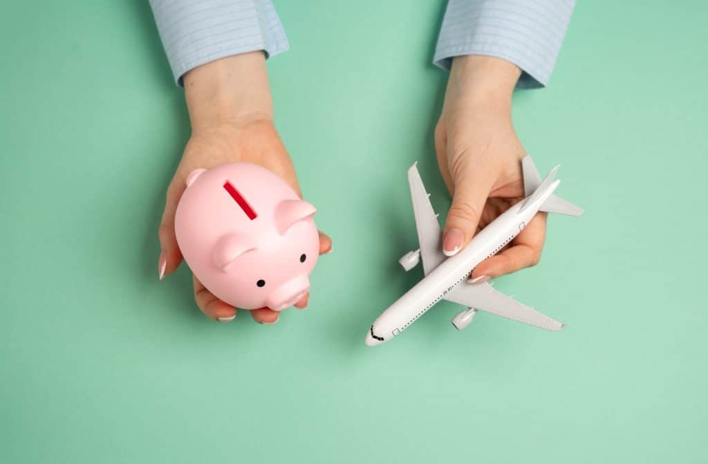 Hands holding a piggy bank and an airplane, illustrating smart flight booking hacks to save money on airfare by switching currencies.