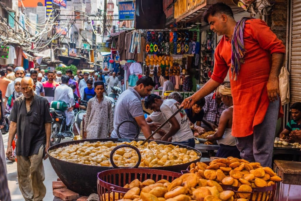 Busy Indian street market with a food vendor frying snacks and crowds of locals, showcasing authentic culture and cuisine when you travel to India.