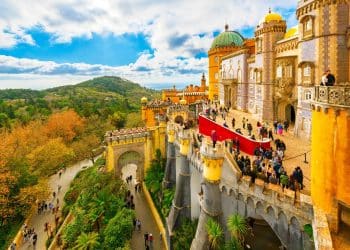 Colorful view of Pena Palace in Sintra, one of the best cities in Portugal, with lush green hills and visitors exploring the historic castle on a bright day.