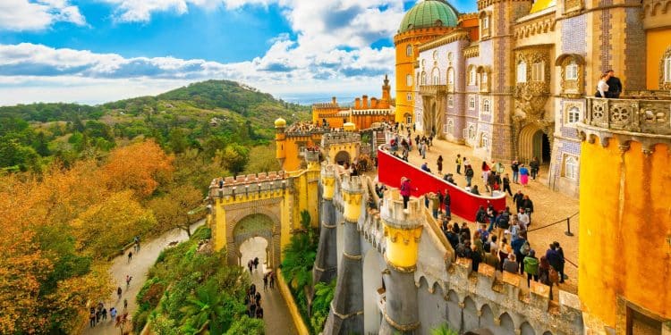 Colorful view of Pena Palace in Sintra, one of the best cities in Portugal, with lush green hills and visitors exploring the historic castle on a bright day.