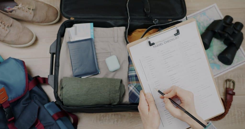 Traveler checking a detailed travel packing checklist beside a suitcase essential for organized and budget-friendly adventures.