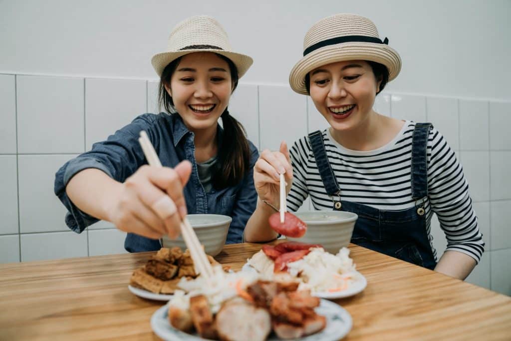 Two female tourists enjoying local food, a strategy to steer clear of common tourist traps at overpriced restaurants.