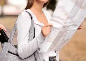 Tourist checking a city map while a pickpocket reaches into her bag, a reminder to stay alert and avoid tourist scams when exploring new places.