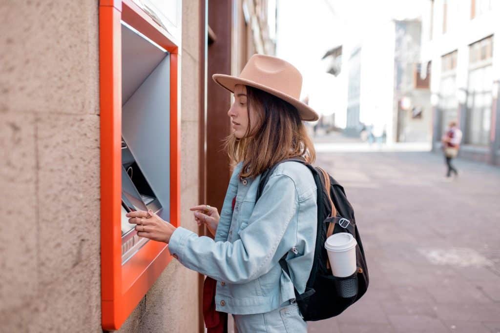 Female traveler using an ATM abroad, illustrating the importance of caution to avoid tourist scams like skimming and card theft.