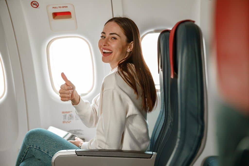 Happy passenger giving thumbs up on airplane seat, enjoying benefits from best travel loyalty programs.