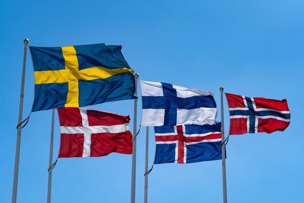 Flags of best Nordic countries to visit waving against a clear blue sky.