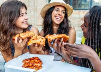 Group of friends laughing and sharing pizza outdoors, showing how budget dining tips make meals affordable and social.