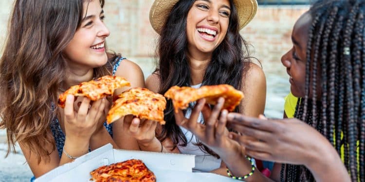 Group of friends laughing and sharing pizza outdoors, showing how budget dining tips make meals affordable and social.