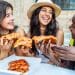 Group of friends laughing and sharing pizza outdoors, showing how budget dining tips make meals affordable and social.