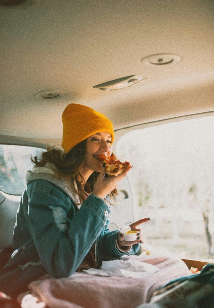 A young girl enjoying pizza in a car, a perfect example of eating cheap food in Europe.