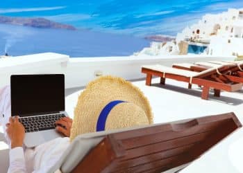 Traveler with a laptop on a sunny terrace overlooking the sea, capturing the lifestyle flexibility that comes with working abroad.