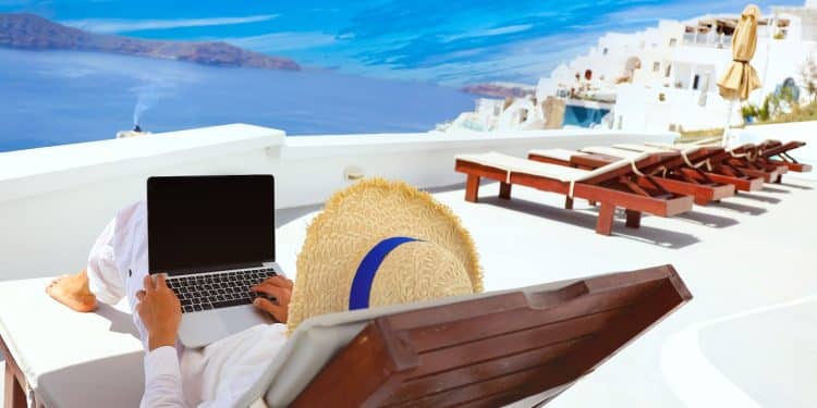 Traveler with a laptop on a sunny terrace overlooking the sea, capturing the lifestyle flexibility that comes with working abroad.