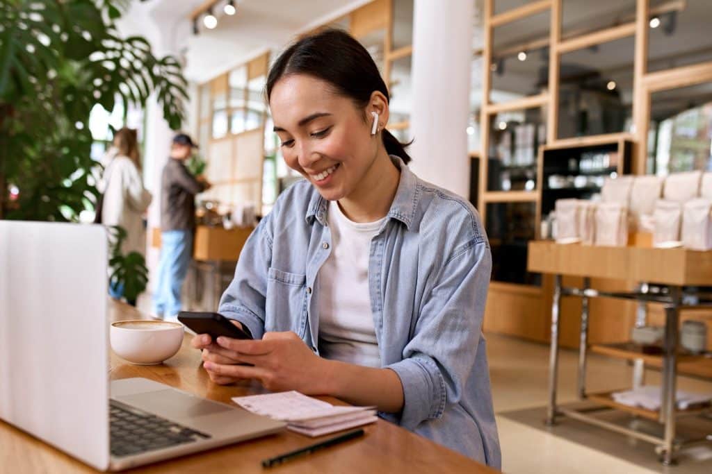 Smiling remote worker at a café using her laptop and phone, reflecting the balance of productivity and community in nomad life.
