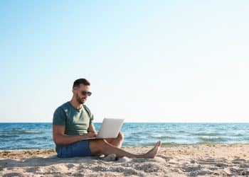 Man working on a laptop at the beach showing the lifestyle connected to digital nomad insurance.
