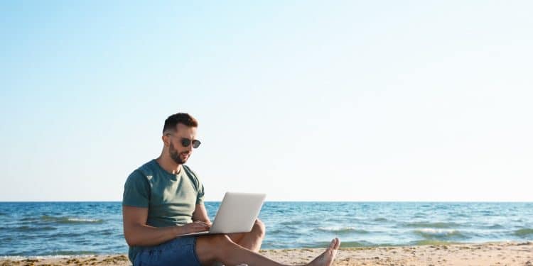 Man working on a laptop at the beach showing the lifestyle connected to digital nomad insurance.