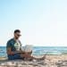 Man working on a laptop at the beach showing the lifestyle connected to digital nomad insurance.