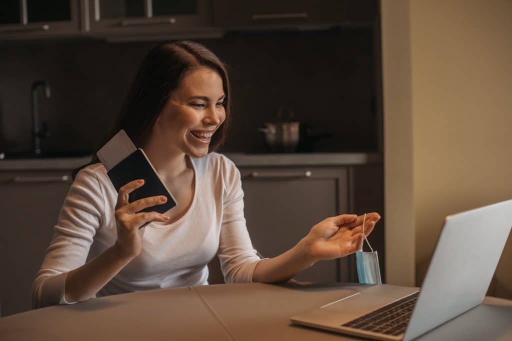 Smiling woman holding a passport while on a video call showing future of digital nomad insurance.