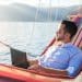 A digital nomad relaxing in a hammock by the sea while working on a laptop, showing how digital nomad productivity tips help balance work and travel.