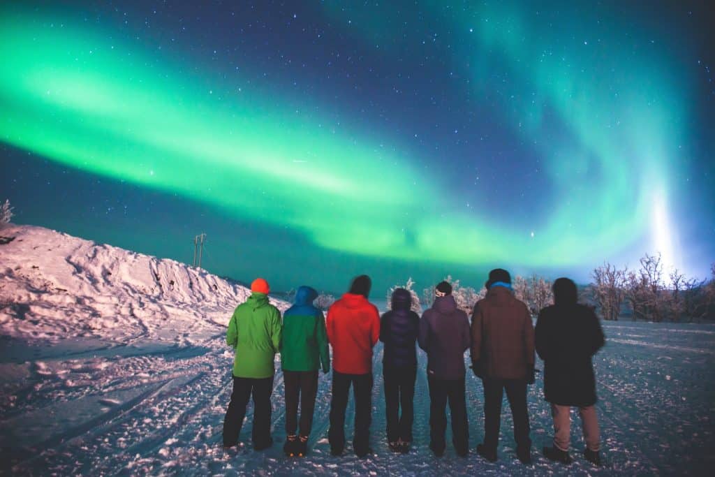 Group of travelers watching the northern lights in winter, a magical moment often experienced on Greenland travel adventures.