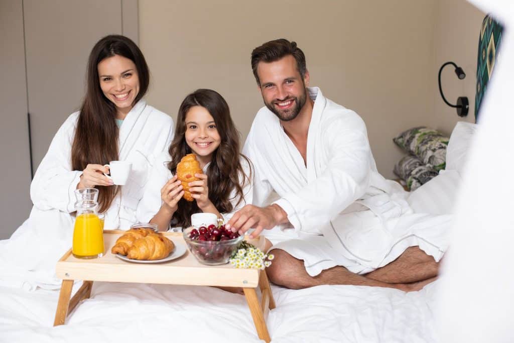 A happy family enjoying their breakfast in bed on their travel using points.