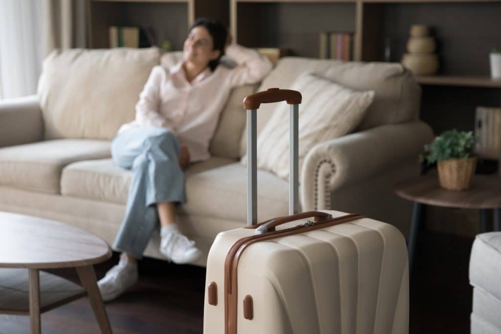 Woman relaxing on a sofa with a suitcase in the living room after arriving at a new home for house sitting.