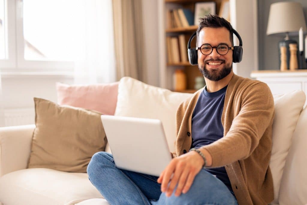 Smiling traveler housekeeping with headphones working on a laptop in a cozy living room.