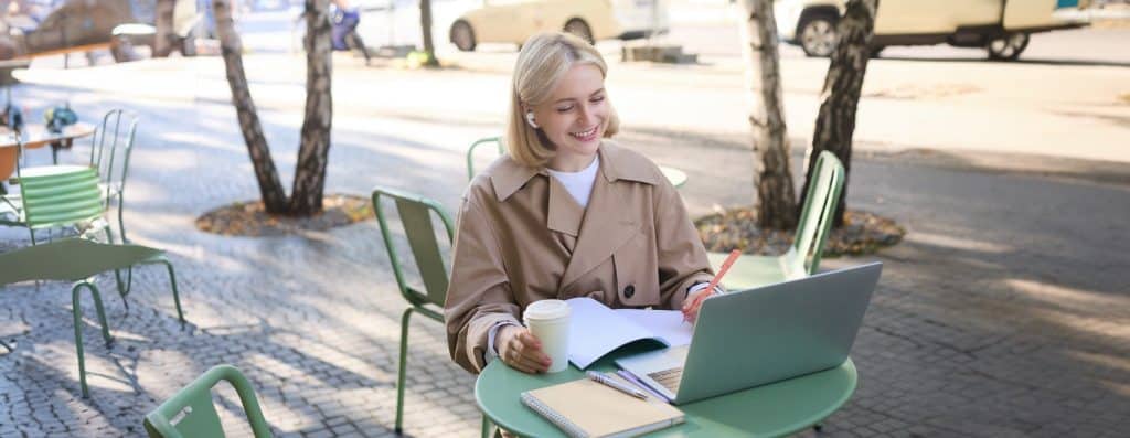 Woman working on laptop at outdoor café, staying online after learning how to get an eSIM.