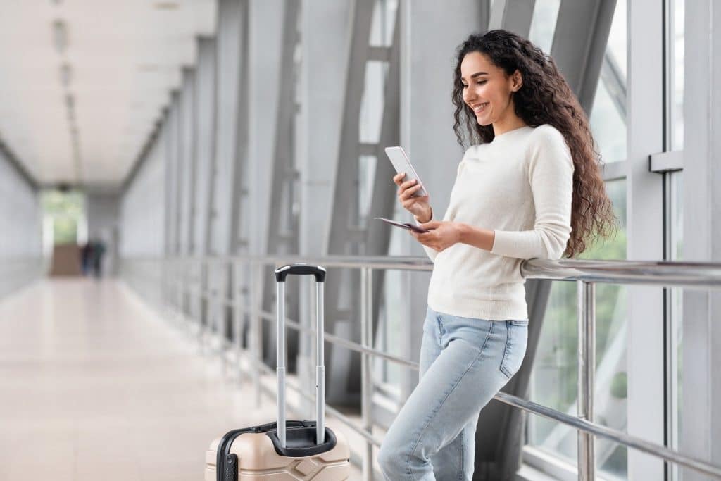 Traveler at airport using smartphone and passport, showing how to get an eSIM while abroad.