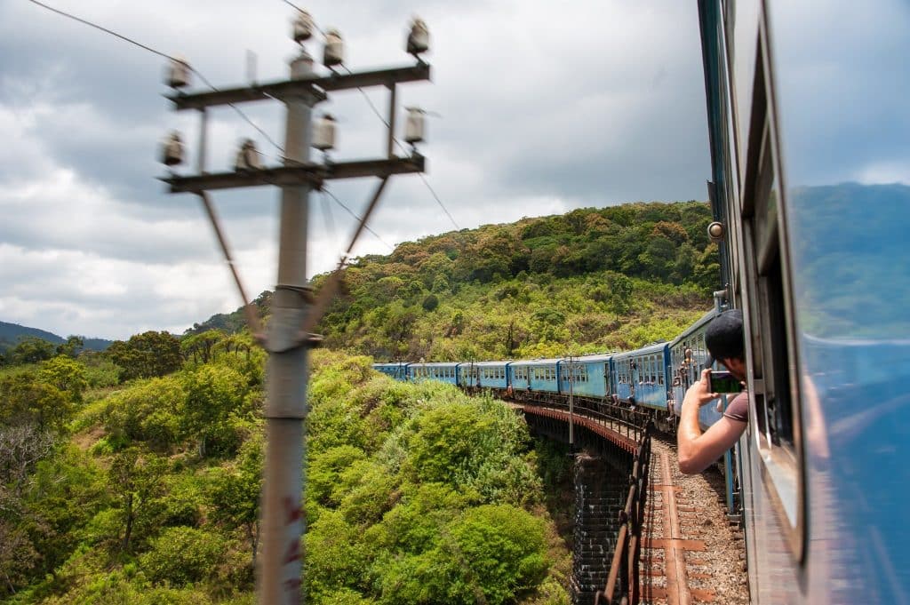 Passengers leaning out of the Kandy to Ella train to photograph sweeping mountain views along the route.