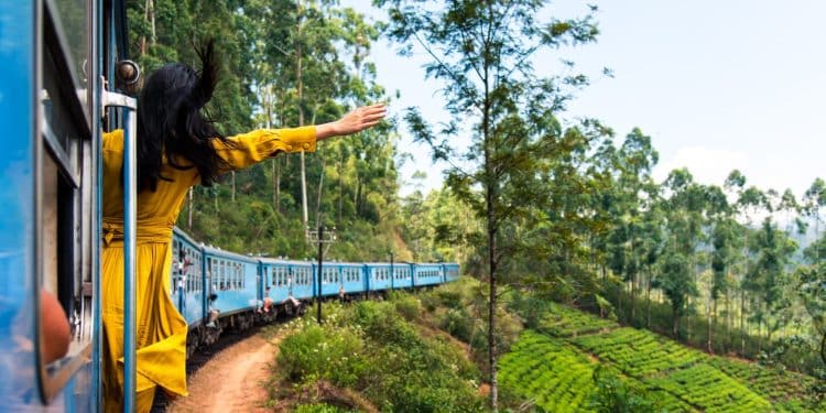 A woman in a yellow dress enjoying the open doorway of the Kandy to Ella train passing through tea plantations.