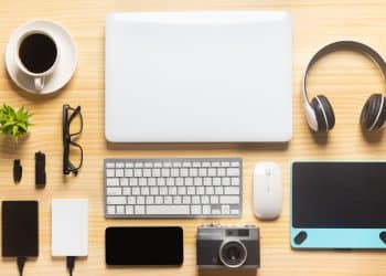 Remote work gear setup with laptop, headphones, camera, and office essentials on a wooden desk.