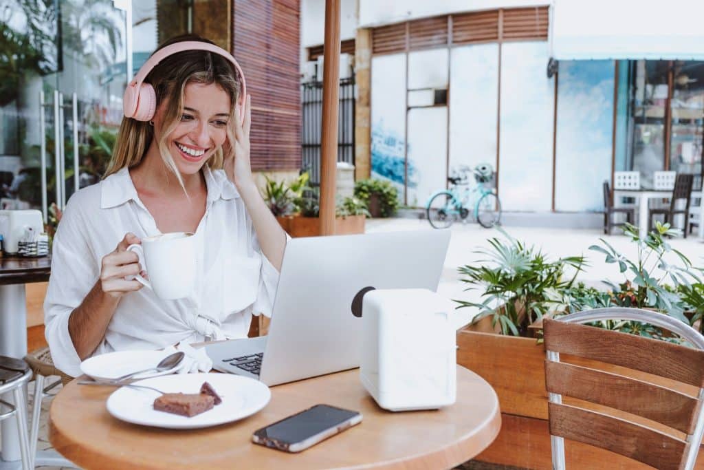 Digital nomad enjoying coffee while using remote work gear at an outdoor café.