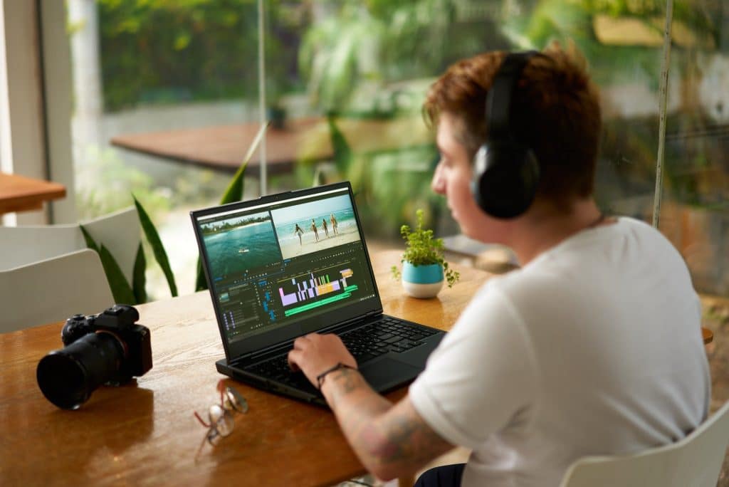 Traveler editing videos on a laptop with remote work gear in a bright workspace.