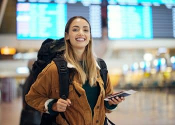 Student traveler smiling with backpack at airport using a student travel discount.