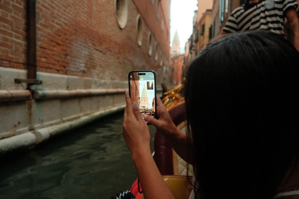 A traveler taking a photo while on a gondola ride during their travel to Venice.