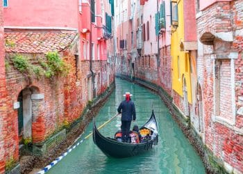 A gondolier guiding his gondola through a quiet canal, a classic view when you travel to Venice.