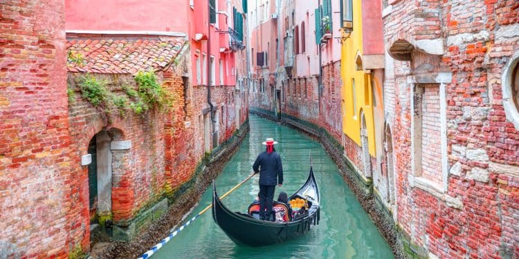 A gondolier guiding his gondola through a quiet canal, a classic view when you travel to Venice.