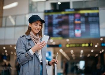 Traveler checking google flights price alerts on phone at an airport departures board
