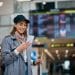 Traveler checking google flights price alerts on phone at an airport departures board