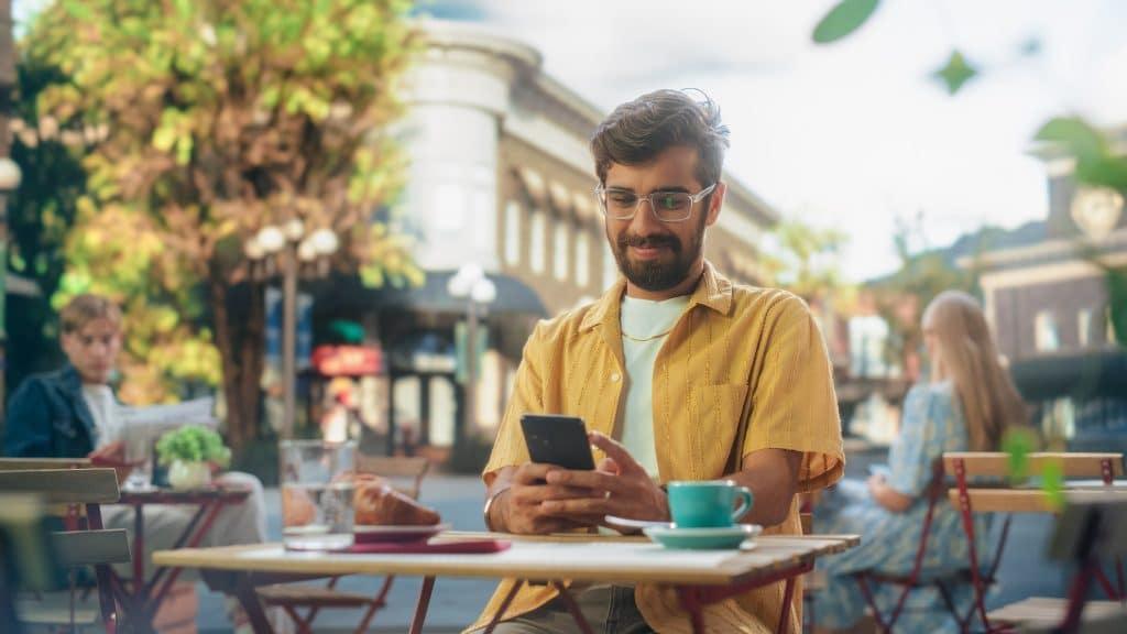 Man reading google flights price alerts notification on a smartphone at an outdoor cafe