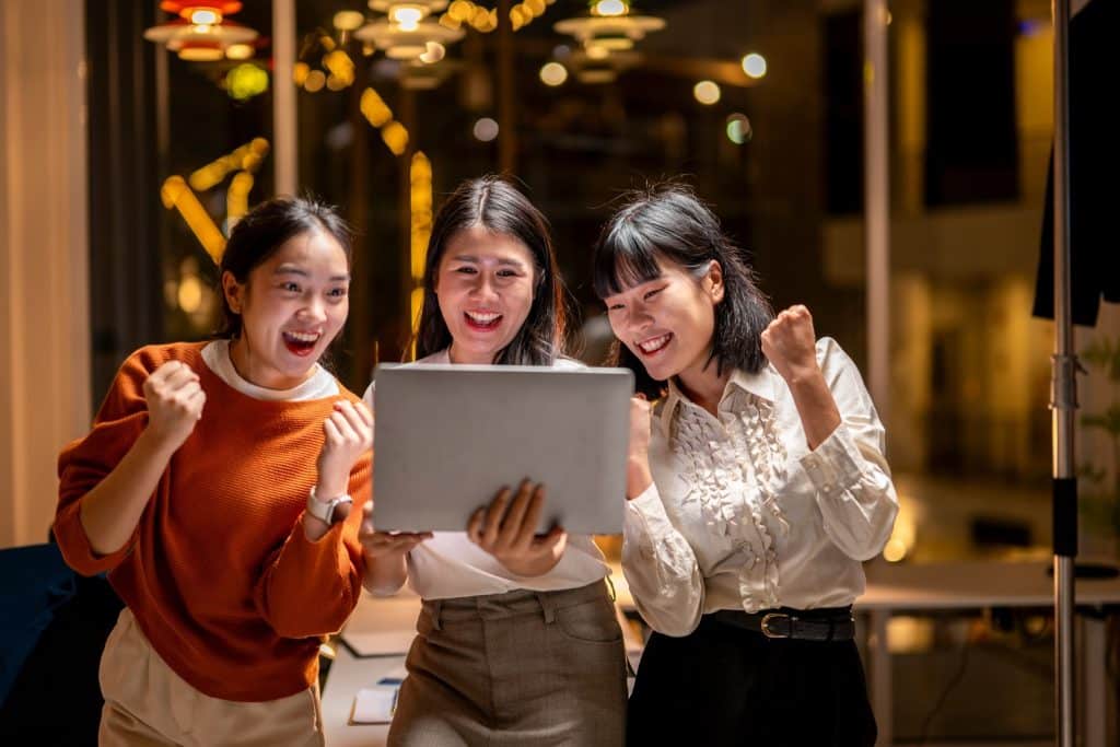 Friends celebrating a flight deal after google flights price alerts drop, booking on a laptop